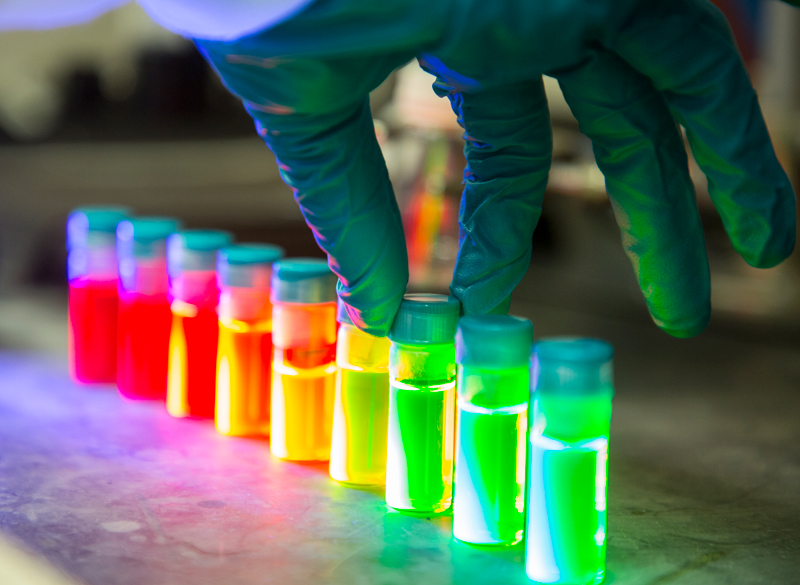 A gloved hand working with glowing vials of different colors