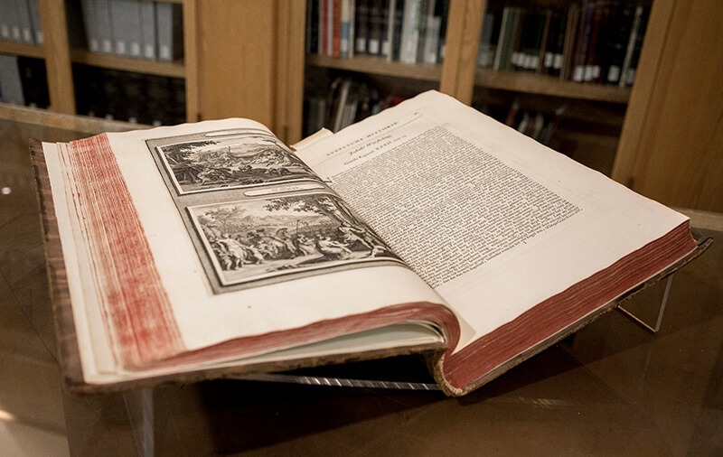 A photo of a large antique book laying open on a glass table