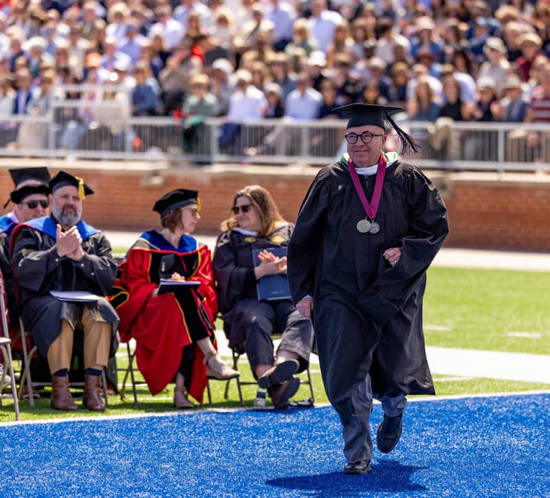 Professor Rob Pocock in academic regalia walking to receive the H.O.P.E. award