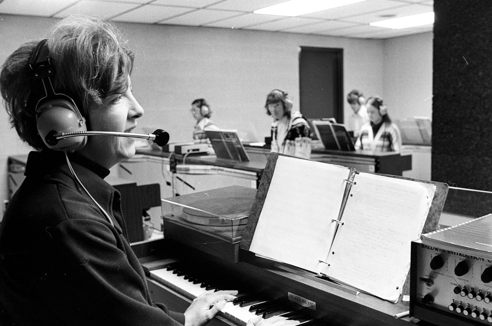 A historic black-and-white photo of Professor Joan Conway teaching class from a piano
