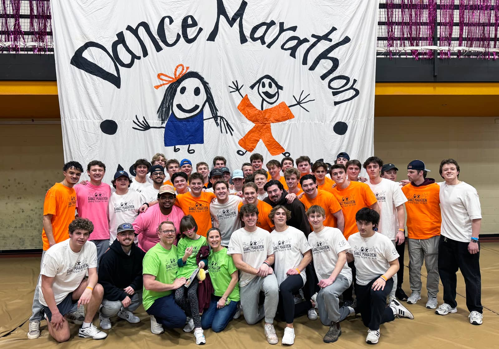 Dance Marathon dancers and students posing in front of a hand-painted Dance Marathon banner