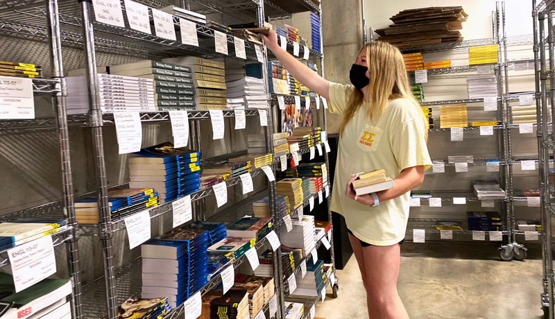 A student standing at a shelf of textbooks