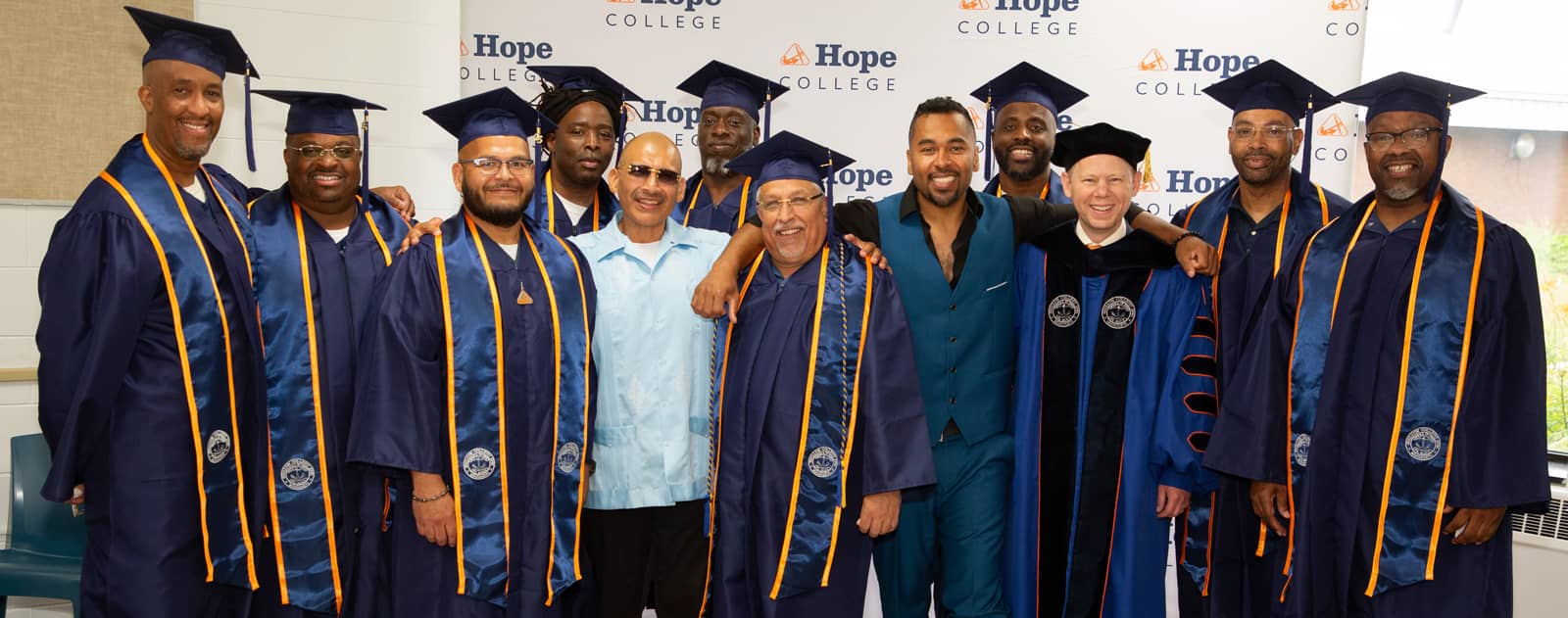 Students from the Hope-Western Prison Education Program posing with Hope College President Matt Scogin in front of a Hope College banner