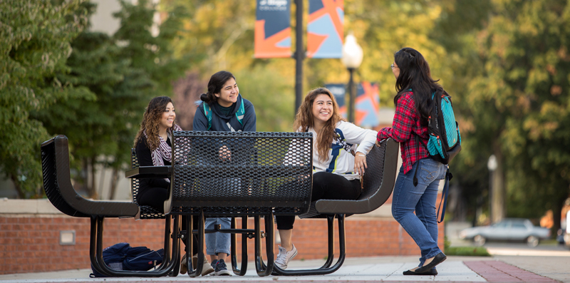 Four female students talking and laughing around an outdoor table